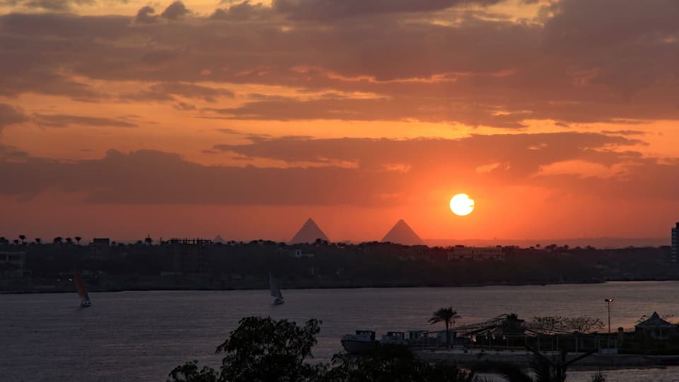 Dramatic fiery red and orange sunset over the River Nile with feluccas calmly sailing and the magnificent Giza pyramids in the background. View from Maadi, Cairo, Egypt.