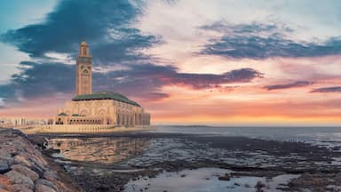Um edifício histórico com uma torre alta, litoral rochoso e céu ao pôr do sol.