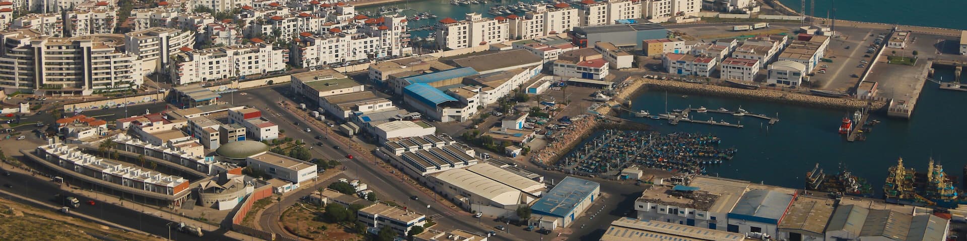 An aerial view of a coastal city with a beach, marina, and dense urban development.