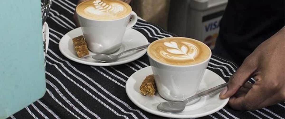 Two cups of coffee with latte art on a striped tablecloth.