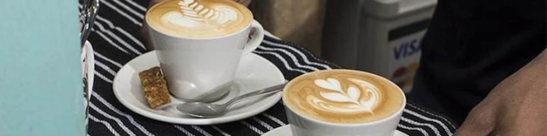 Two cups of coffee with latte art on a striped tablecloth.