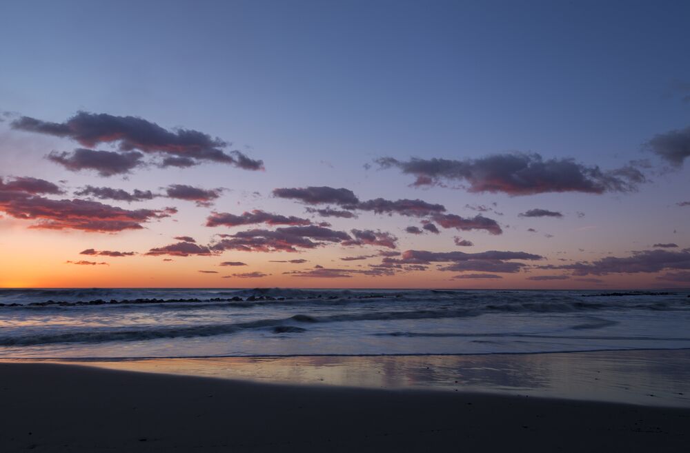 A beach at sunset with waves and scattered clouds.
