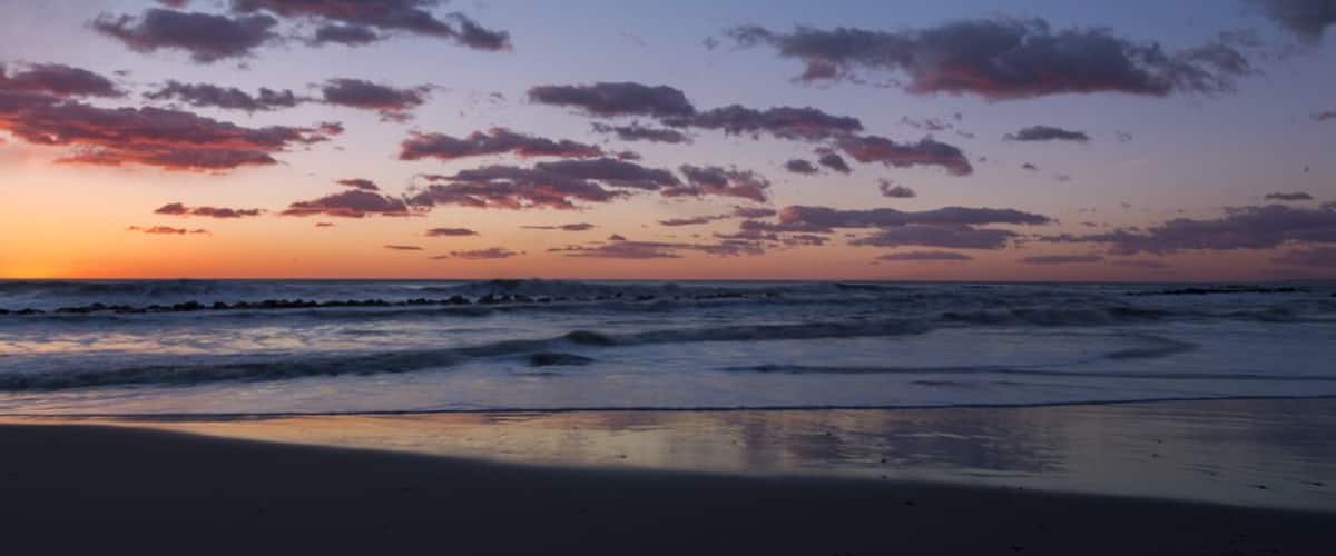 A beach at sunset with waves and scattered clouds.