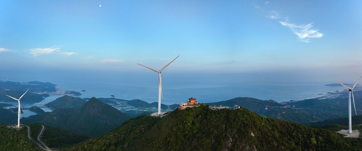 Un paisaje montañoso con aerogeneradores y un edificio tradicional en una colina.