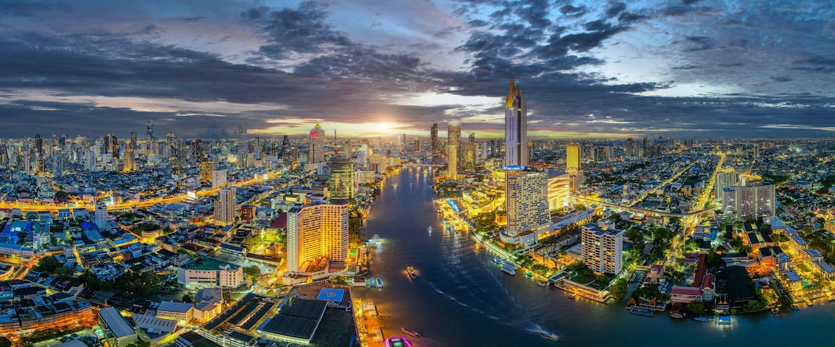 A cityscape at dusk with a river running through it, illuminated buildings, and a prominent skyscraper.