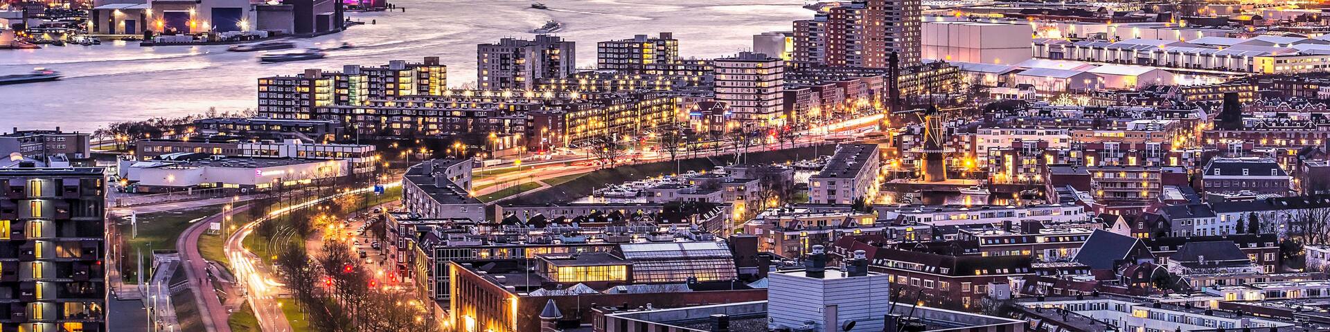 A cityscape at dusk with a river, industrial buildings, and a bridge.