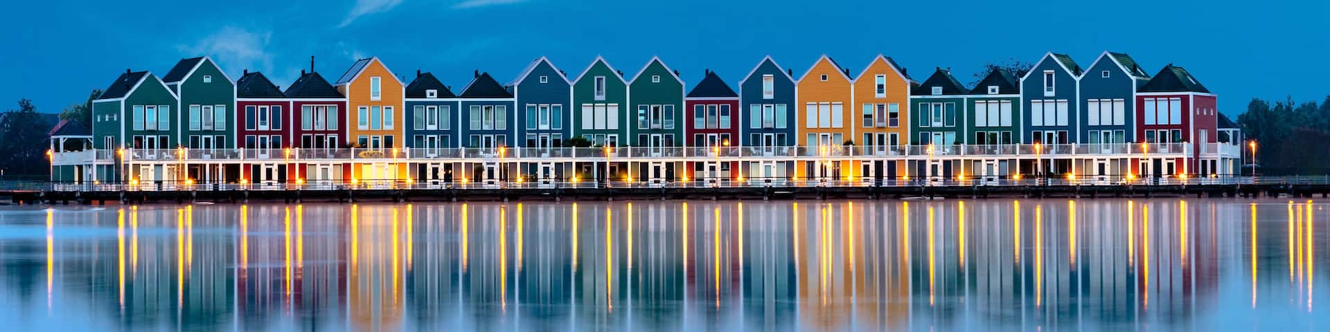 A row of colorful houses by a calm body of water at dusk.