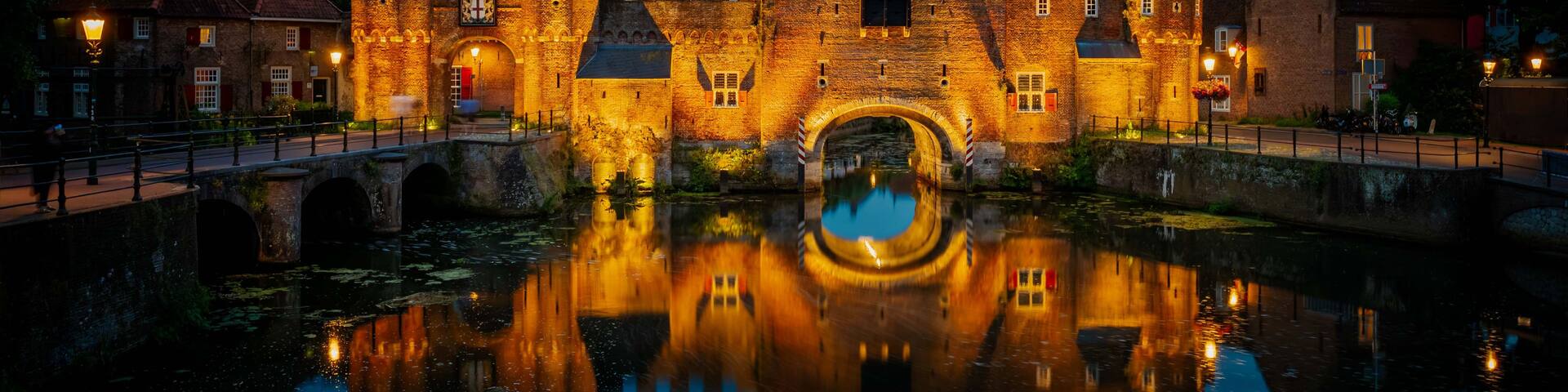 A historic castle with a moat and a bridge, reflecting the structure and the sky.