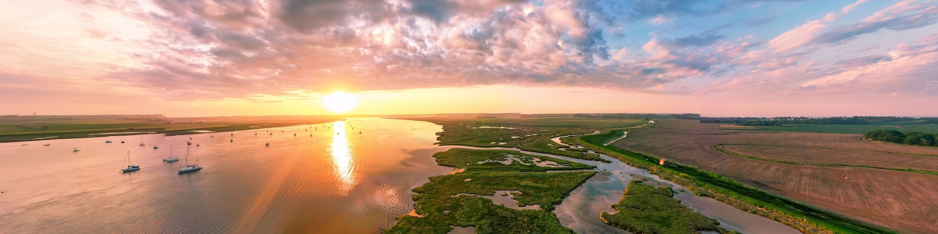 Um rio com barcos, um pôr do sol e uma paisagem com vegetação verde e campos.