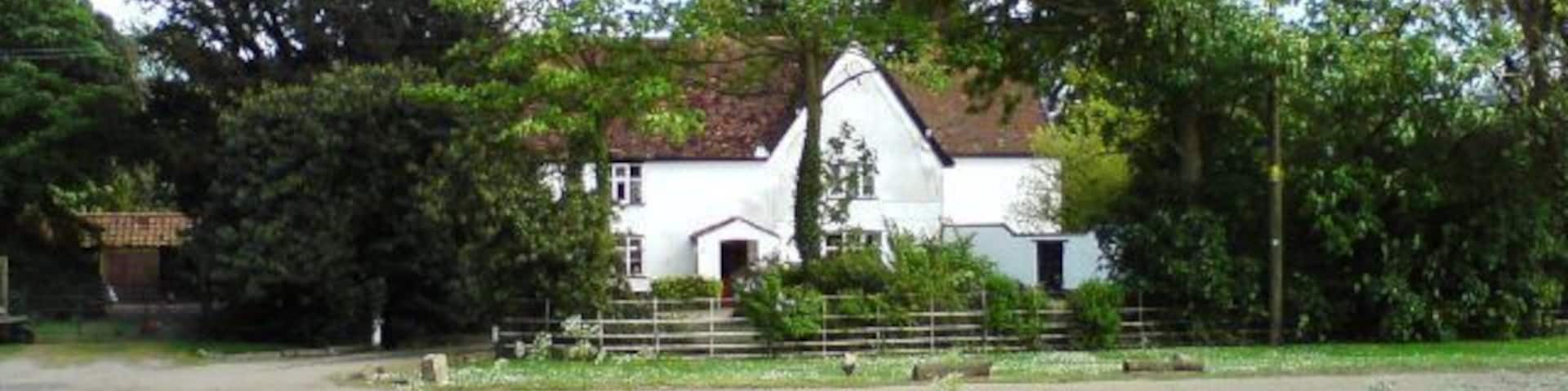 A white house with a red roof, surrounded by green fields and trees.