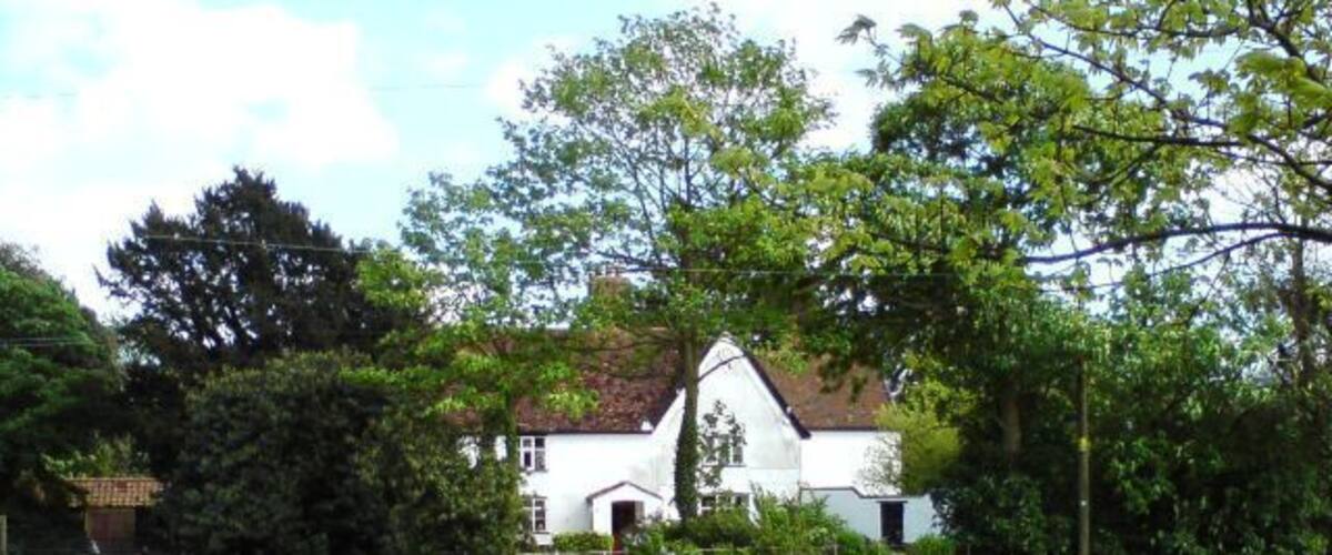 A white house with a red roof, surrounded by green fields and trees.
