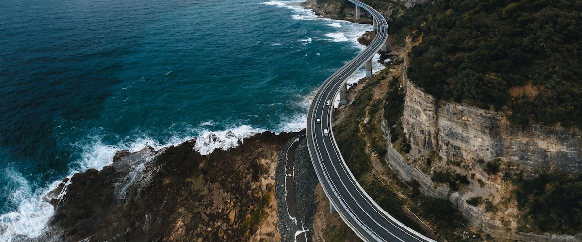 Una carretera costanera serpegen al costat d'un penya-segat, amb vista al mar.