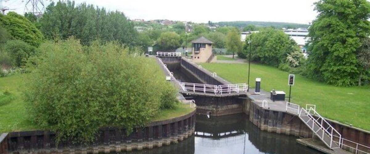 A lock system with a small building, surrounded by greenery and a calm river.