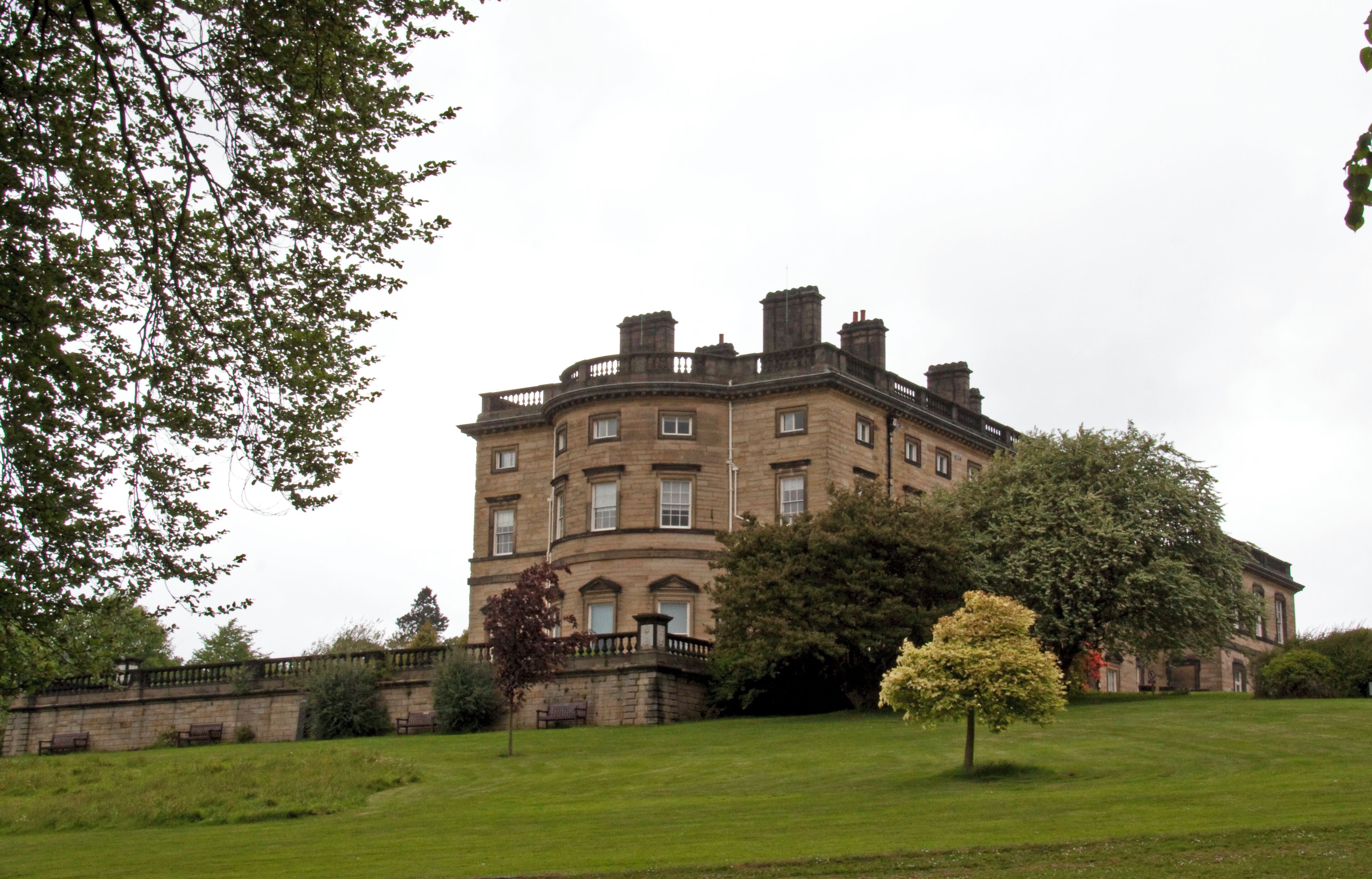 A large, historic building with a curved facade, surrounded by well-maintained lawns and mature trees.