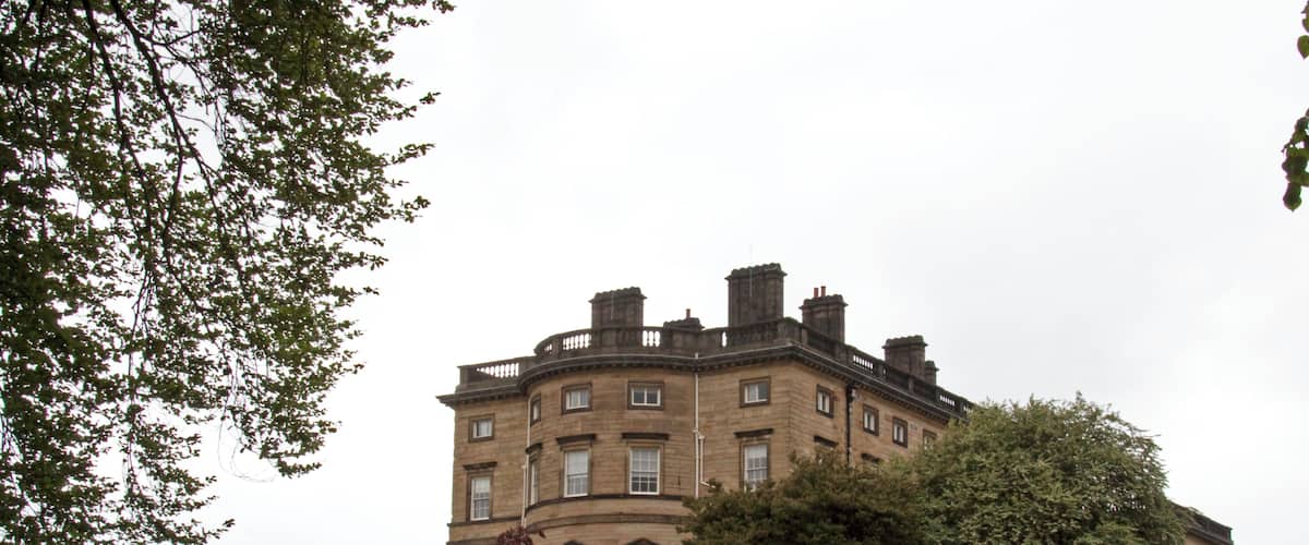 A large, historic building with a curved facade, surrounded by well-maintained lawns and mature trees.
