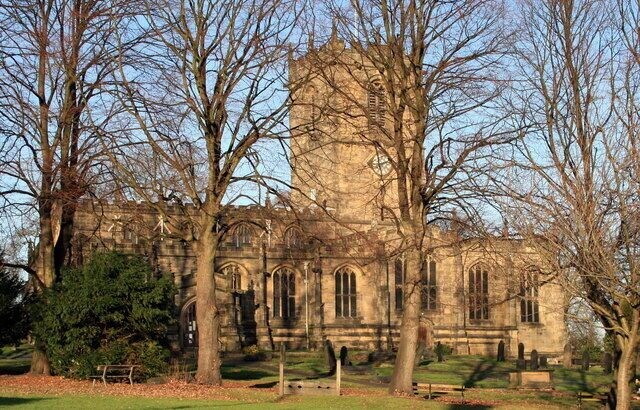 A historic stone building with arched windows and a tower, surrounded by leafless trees.