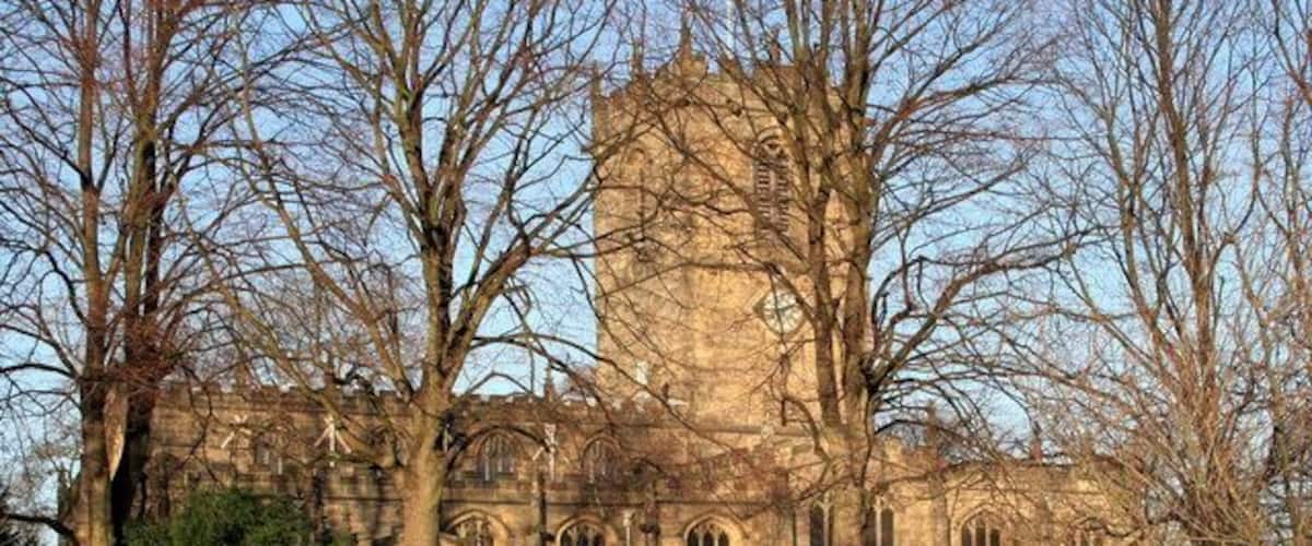 A historic stone building with arched windows and a tower, surrounded by leafless trees.