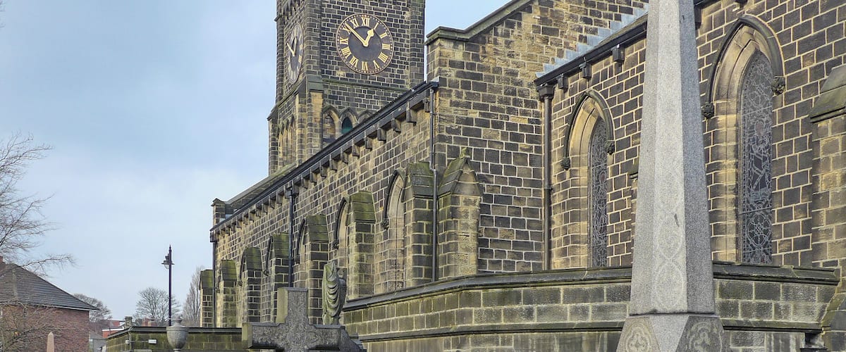 A historic church with a clock tower and multiple gravestones in the foreground.
