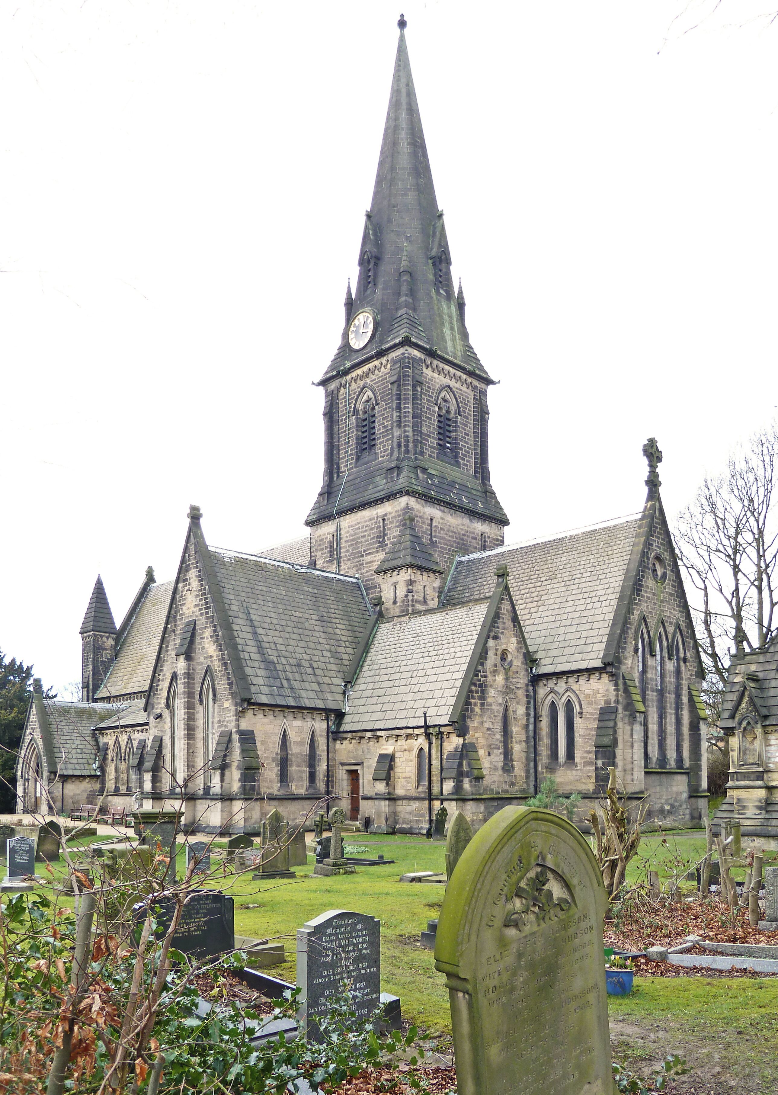 A church with a tall spire and a clock. There are gravestones in the foreground.