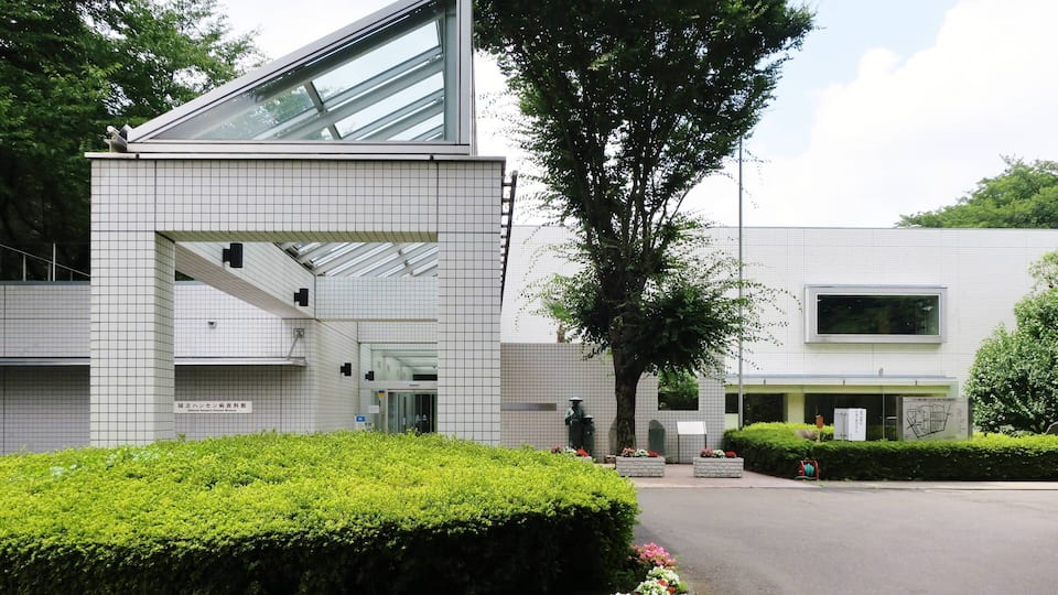 A modern building with a tiled facade, a large tree, and a well-maintained garden with flowers.