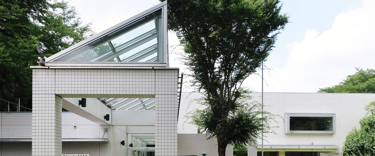 A modern building with a tiled facade, a large tree, and a well-maintained garden with flowers.