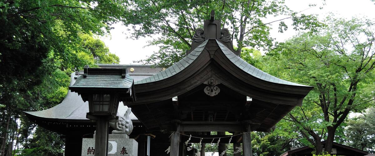 A traditional Japanese pavilion with a curved roof, surrounded by lush greenery and trees.