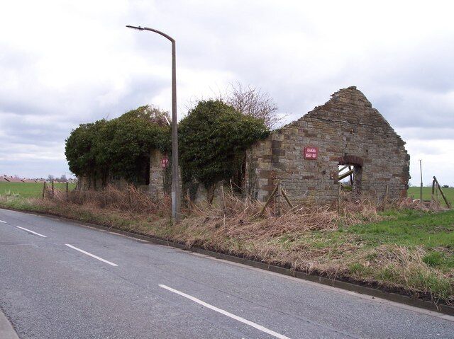 A dilapidated stone building with a red sign, a road, and a lamppost.