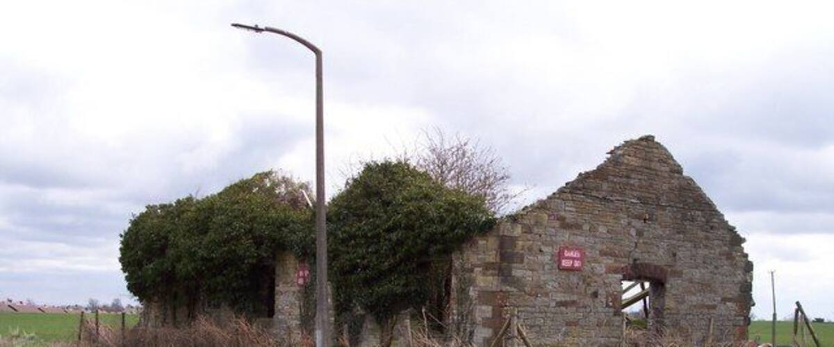 A dilapidated stone building with a red sign, a road, and a lamppost.
