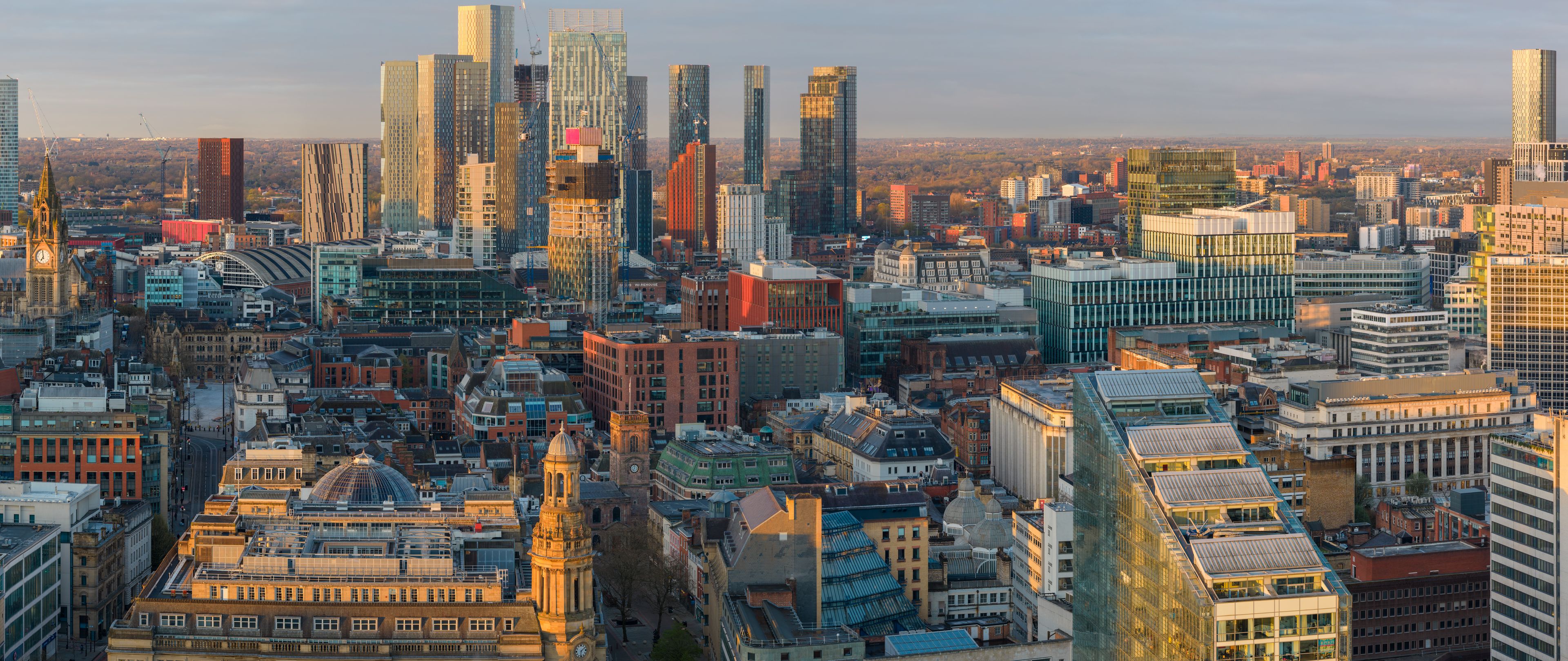 A beautiful  aerial panorama of Manchester city centre at golden hour. Sun hits modern skyscrapers and historic landmarks under a warm morning sky.