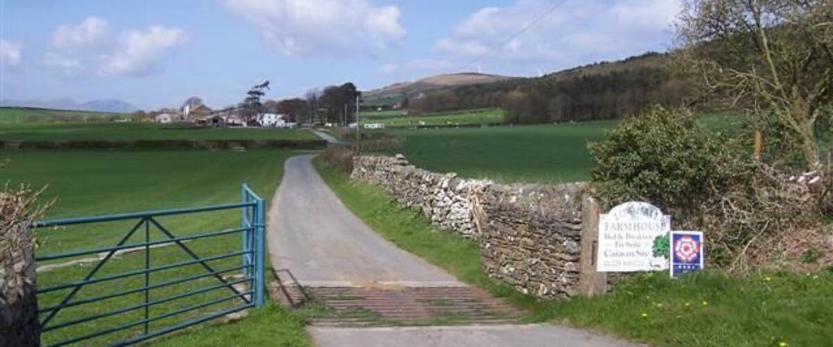 A rural road leading to a farmhouse with a stone wall and a blue gate.