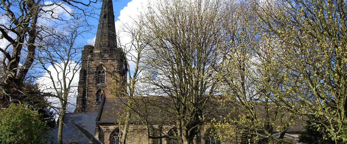 A church with a tall spire, surrounded by trees and a fence.