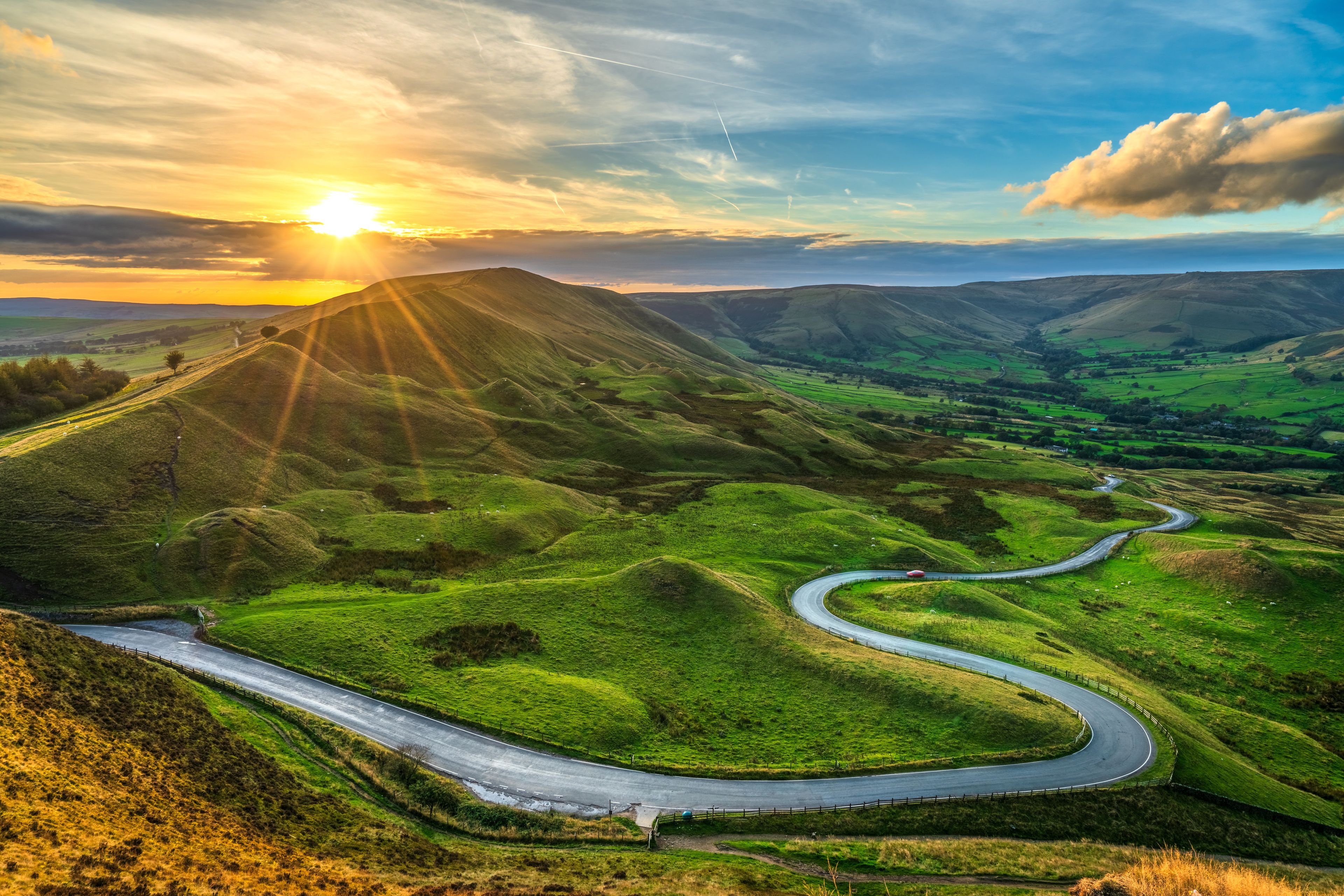 A winding road through rolling green hills with a sunset in the background.