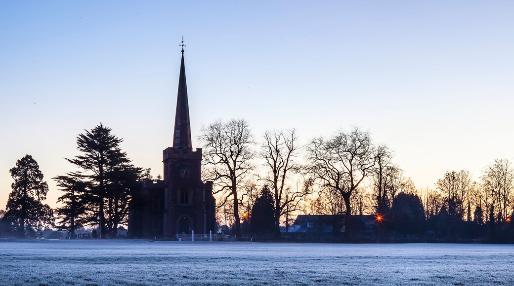 A church spire silhouetted against a sunset, a frost-covered field, and leafless trees.