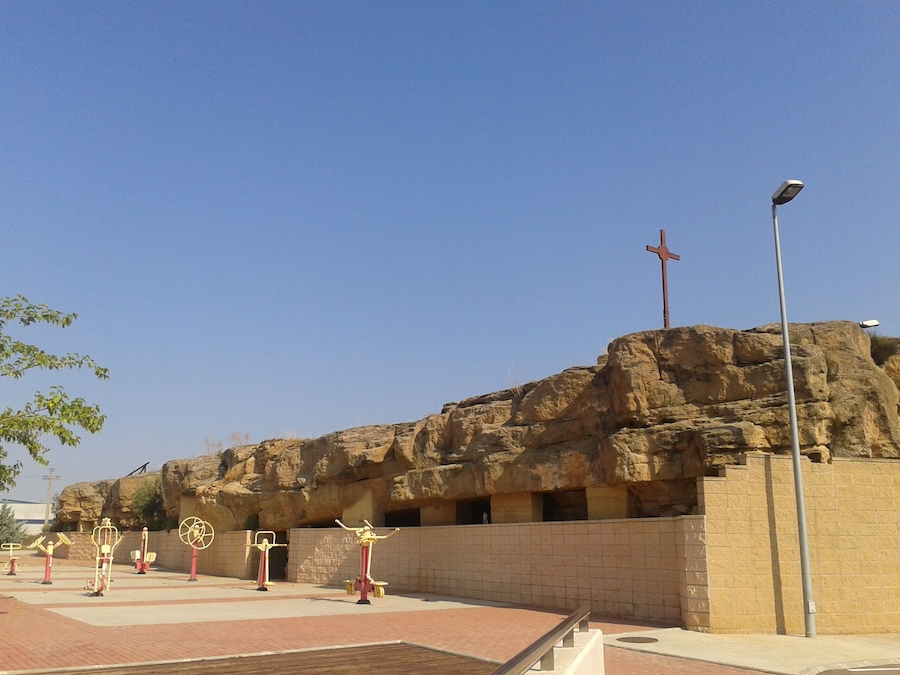 A rocky outcrop with a cross on top, outdoor exercise equipment, and a paved area.