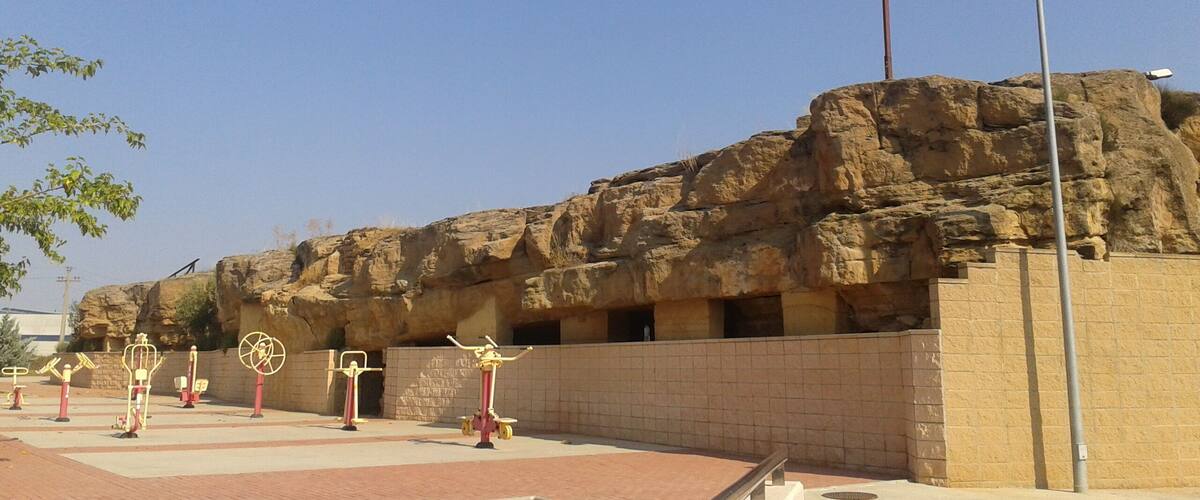 A rocky outcrop with a cross on top, outdoor exercise equipment, and a paved area.
