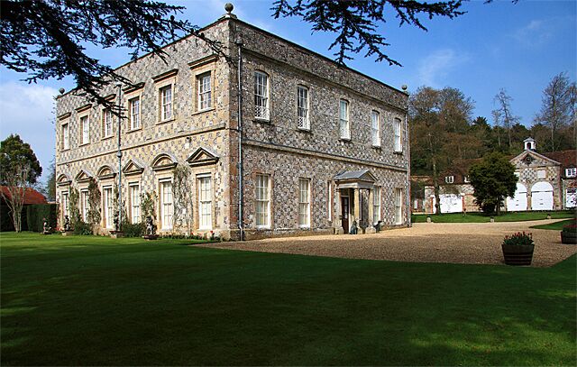 A large stone building with arched windows and a central entrance, surrounded by a well-maintained lawn and trees.