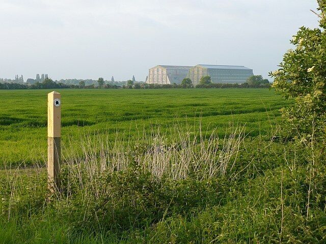 A green field with a wooden post and a modern building in the background.