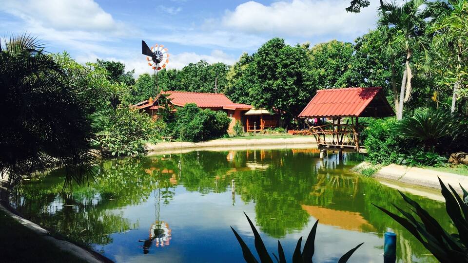 A serene pond with a windmill and traditional buildings surrounded by lush greenery.