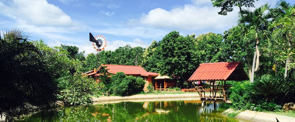 A serene pond with a windmill and traditional buildings surrounded by lush greenery.