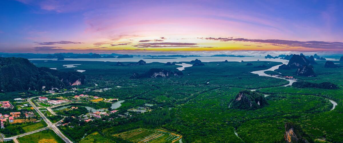 A lush green landscape with winding rivers, a variety of vegetation, and distant mountains under a colorful sunset sky.