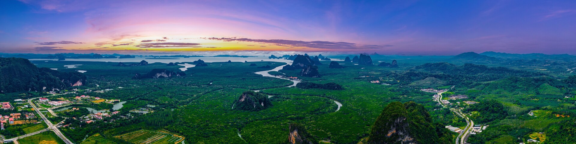 A lush green landscape with winding rivers, a variety of vegetation, and distant mountains under a colorful sunset sky.