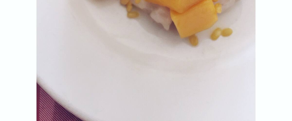 A plate of rice topped with yellow mango cubes and a small amount of peanuts.