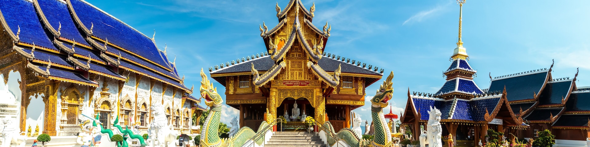 Panorama of Thai Buddhist temple with blue tiled roof and statues