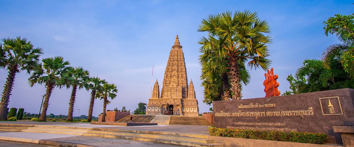 A temple with a tall spire, palm trees, and a stone monument with inscriptions.