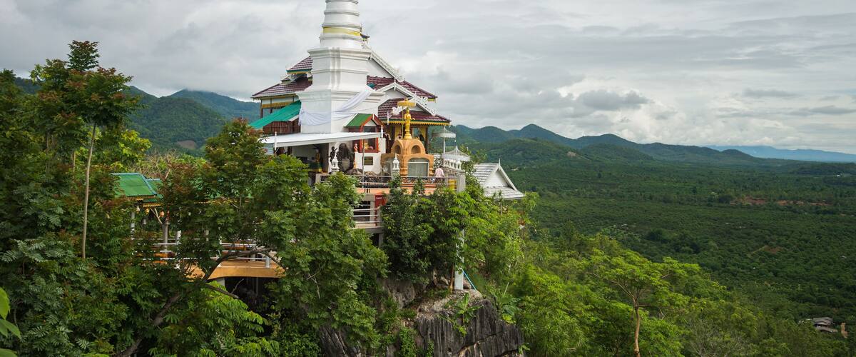 A white temple with a tall spire, surrounded by lush green mountains and trees.