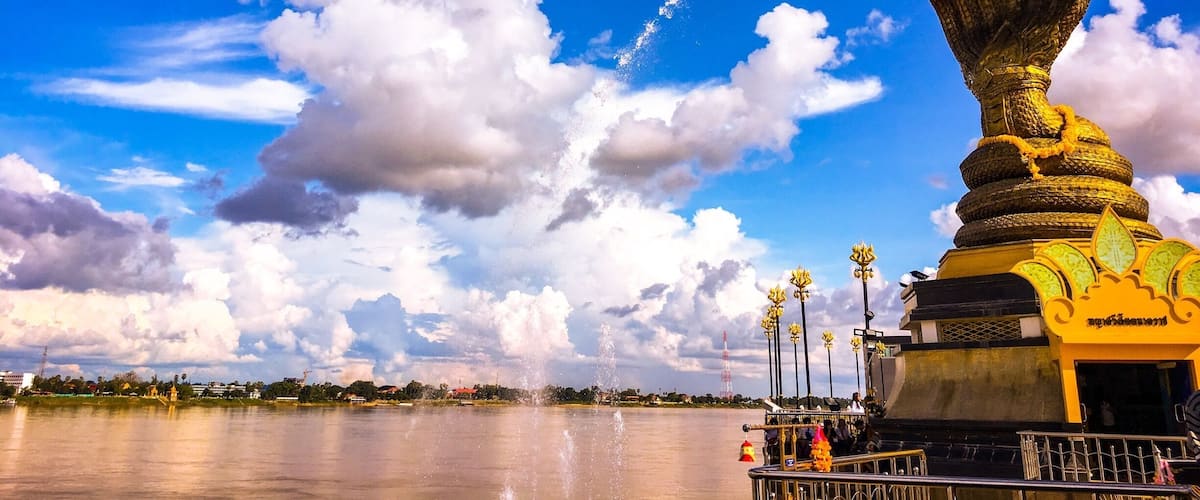 A golden statue with a snake, a body of water, and a clear sky with clouds.