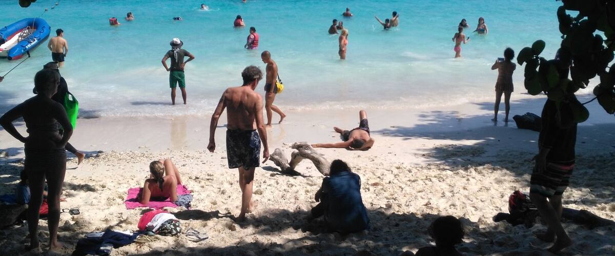 A beach with people swimming and sunbathing, boats in the water, and a clear blue sky.