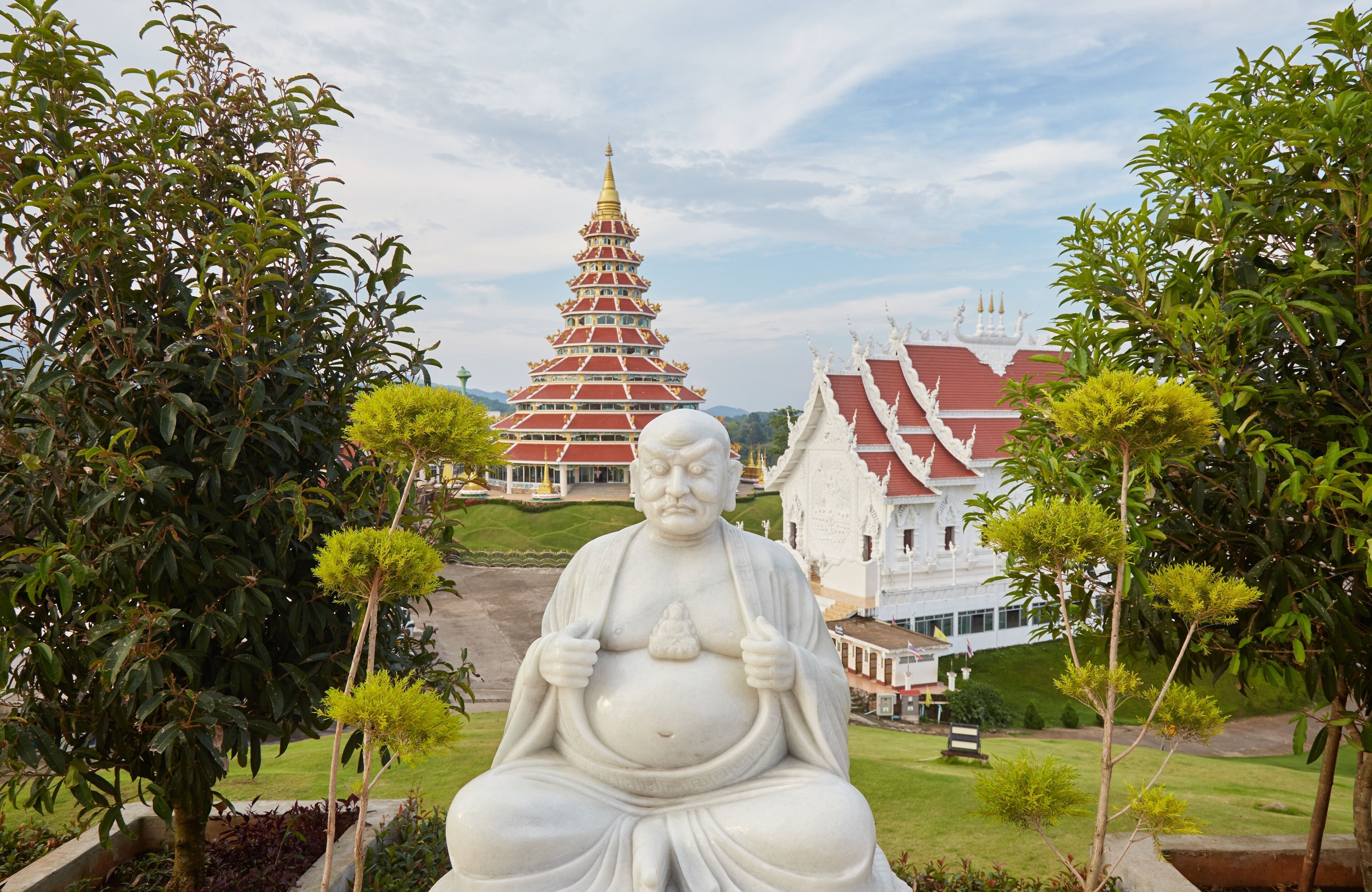 A large Buddha statue in a garden with a pagoda in the background.