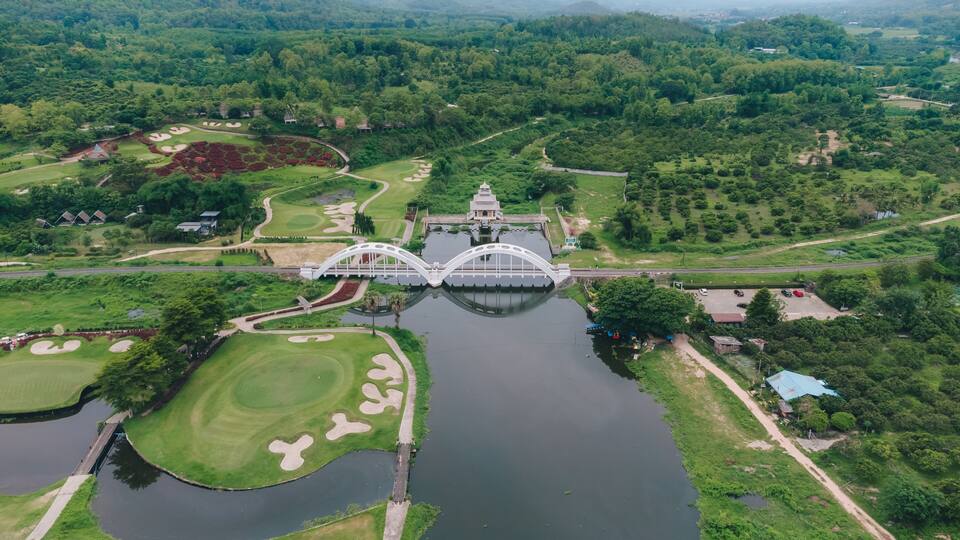 An aerial view of a golf course with a bridge, water body, and surrounding greenery.