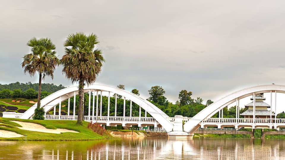 A white bridge with a pagoda-like structure on top, palm trees, and a red train on the tracks.